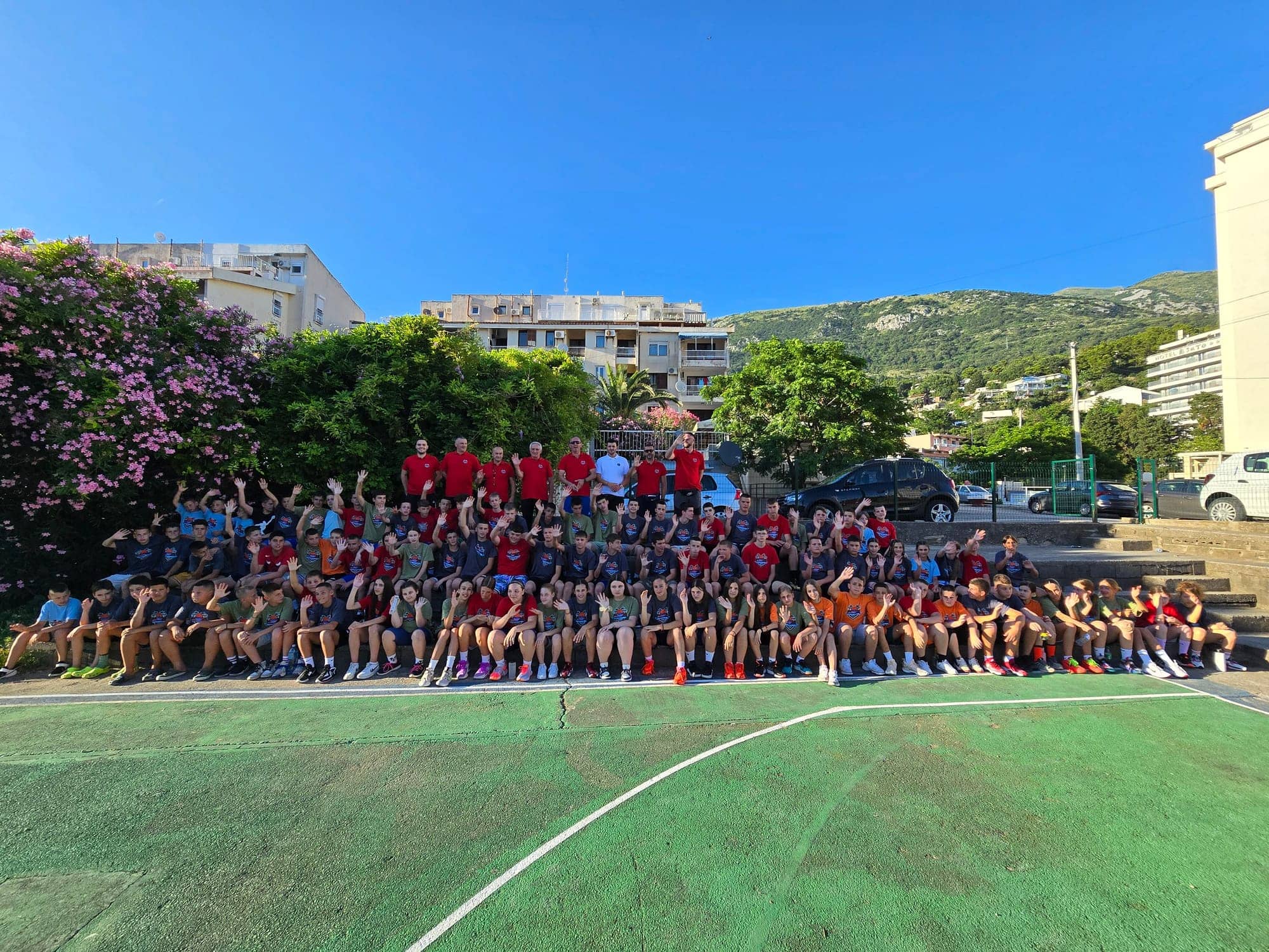 The whole camp — campers and coaches waving from the court, mountains and Sutomore behind