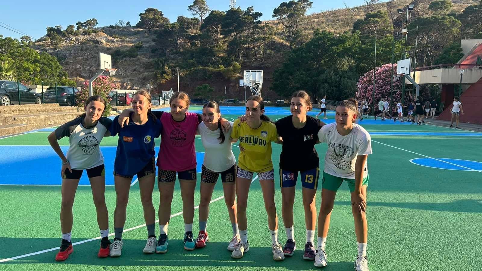 A group of girls on the blue-and-green courts, the hill above Sutomore behind