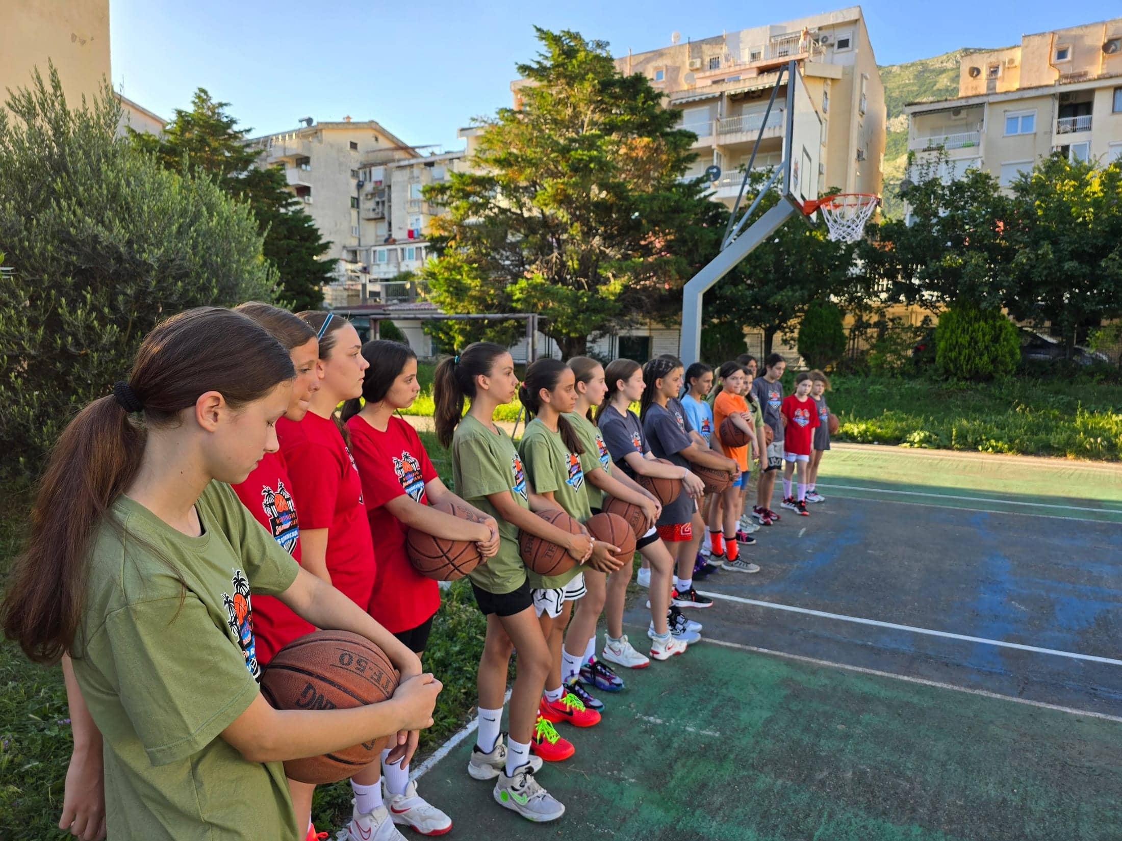 Girls lined up along the court with basketballs in golden light
