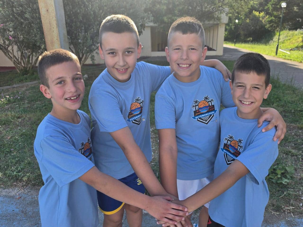 Four boys in camp shirts stacking hands in the middle, golden light in front of the accommodation