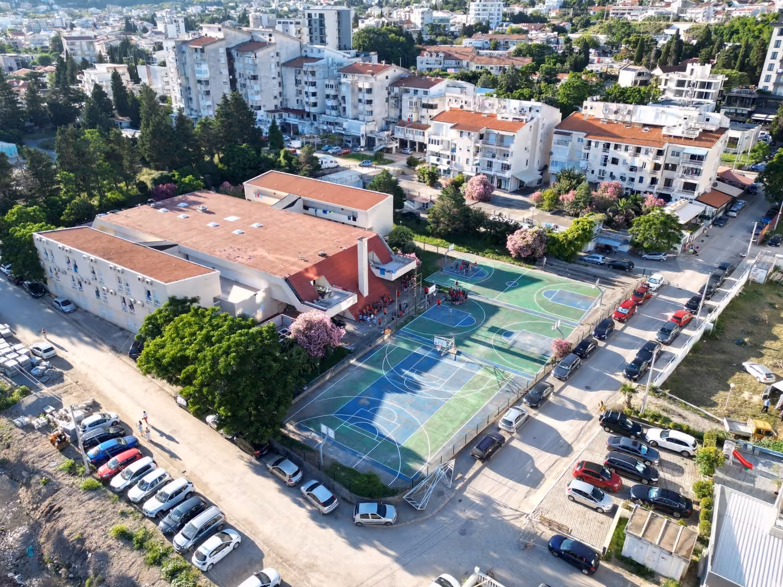 Aerial view of the camp — accommodation next to two basketball courts, the town of Sutomore and the sea behind